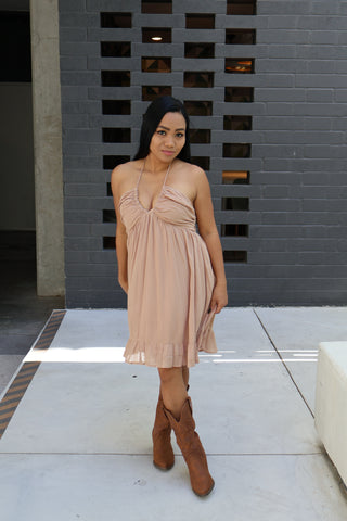 Woman in a beige dress and brown boots standing in front of a textured wall.
