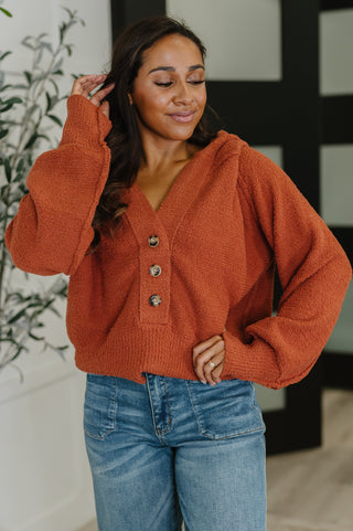 Woman wearing a rust-colored sweater with button details and blue jeans indoors.