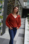 Woman wearing a red sweater and blue jeans standing in a modern indoor setting with geometric wall patterns.
