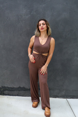 Woman wearing a brown jumpsuit against a dark gray wall.