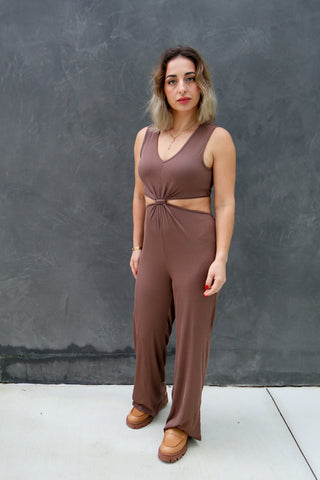 Woman wearing a brown jumpsuit standing against a gray wall.