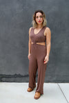 Woman wearing a brown jumpsuit standing against a gray wall.