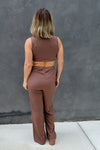 Person wearing a brown outfit standing against a gray wall.