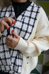 Person wearing a black and white checkered vest over a cream sweater with a geometric patterned background.