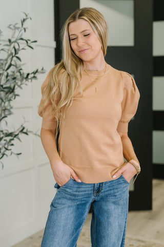 Woman wearing a beige sweater and blue jeans standing indoors.