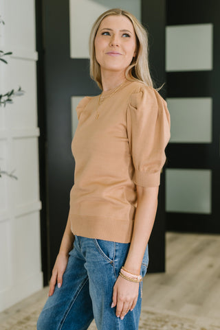 Woman wearing a beige sweater and blue jeans standing indoors.