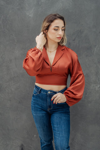 Woman wearing a rust-colored blouse and blue jeans against a gray background