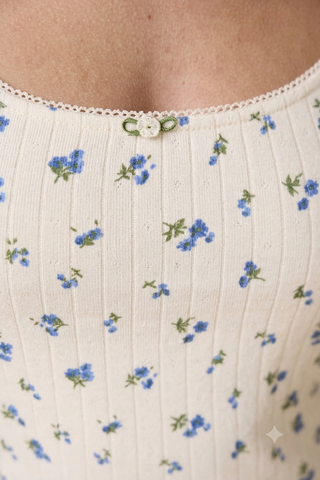 Close-up of a ribbed knit top with a small blue floral print on an off-white base, featuring a delicate lace neckline and a decorative button closure.