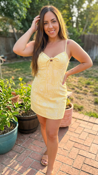 Woman in a yellow dress standing outdoors on a brick patio with plants in the background