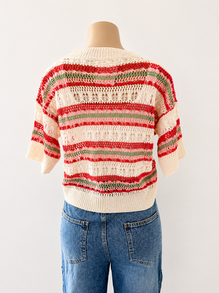 A cream-colored knit sweater with horizontal red and green stripes, displayed on a mannequin torso wearing blue jeans against a plain white background.