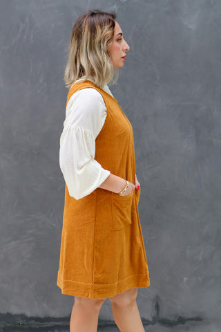 Woman wearing a mustard yellow dress over a white shirt against a gray background