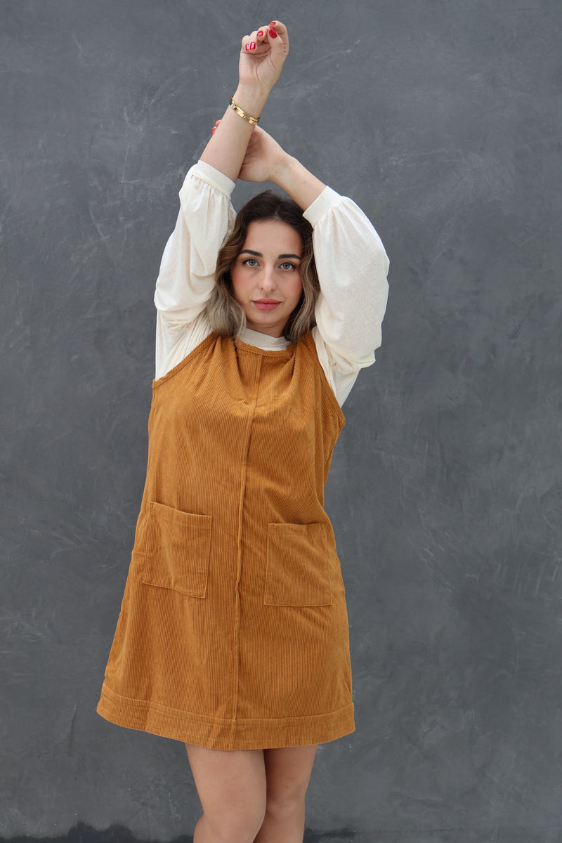 Woman wearing a mustard-colored dress over a white shirt against a dark background