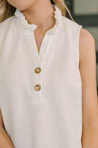 White sleeveless top with gold buttons worn by a person