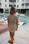 Woman standing by a poolside with a building and palm tree in the background