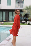 Woman in a red dress standing by a pool with a modern building in the background