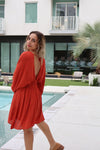 Woman in a red dress standing by a pool with a modern building in the background