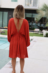 Woman in a red dress standing by a poolside.