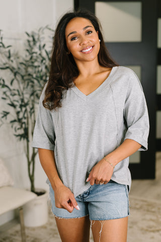 A woman wearing a light gray heathered v-neck t-shirt and denim shorts, standing in a brightly lit indoor setting.