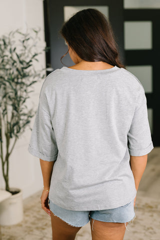 A woman viewed from behind wearing an oversized light gray heather t-shirt and denim shorts in an indoor setting.