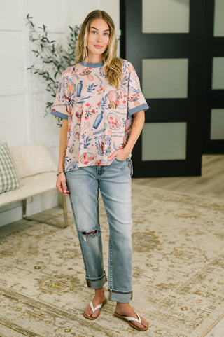 Woman wearing a floral blouse and jeans standing in a room with a couch and plant.