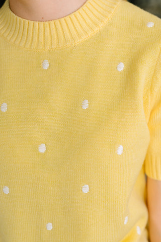 Close-up of a yellow knit top with small white polka dots, showing the ribbed crew neck and short sleeves.