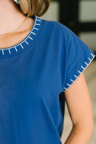 Close-up of a person wearing a royal blue short-sleeve top with white contrast stitching along the neckline and sleeve cuffs.