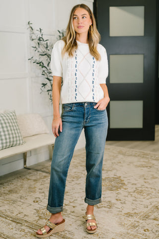 Woman wearing a white blouse with black patterns and blue jeans indoors.