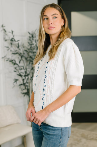 Woman wearing a white sweater with blue accents in an indoor setting