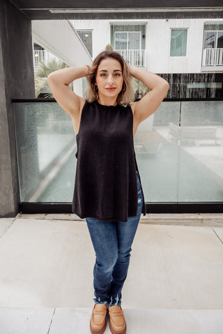 Woman wearing a black sleeveless top and blue jeans standing in front of a modern building.