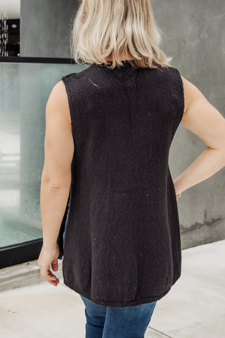 Person wearing a black sleeveless sweater vest outdoors.