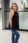 Woman wearing a black sleeveless top and blue jeans standing outdoors.