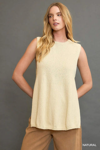 Woman wearing a beige sleeveless top and brown pants against a gray background