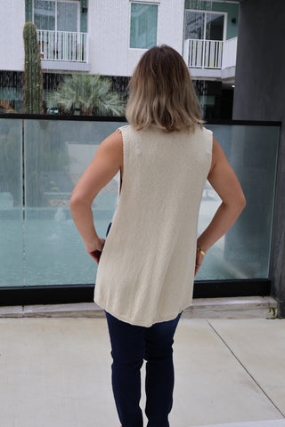 Person wearing a beige sleeveless top and dark pants standing on a balcony.