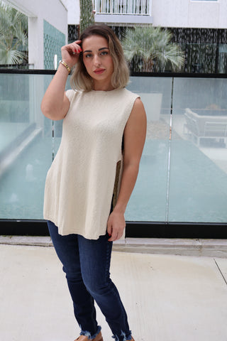 Woman wearing a white sleeveless top and blue jeans standing in front of a glass wall.