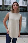Woman wearing a beige sleeveless top and dark pants standing in front of a glass wall.