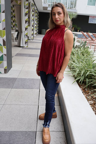 Person wearing a red top and blue jeans standing on a tiled floor with a geometric patterned wall in the background.