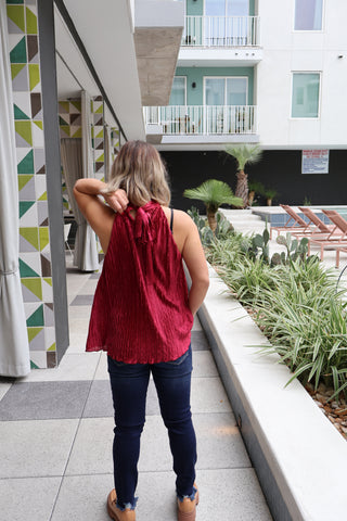 Person wearing a red top and blue jeans standing on a staircase with a geometric patterned wall.