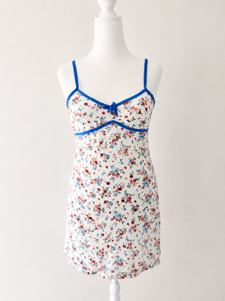 A white camisole nightgown with a red and blue floral print, featuring bright blue trim and thin shoulder straps, displayed on a white mannequin torso.