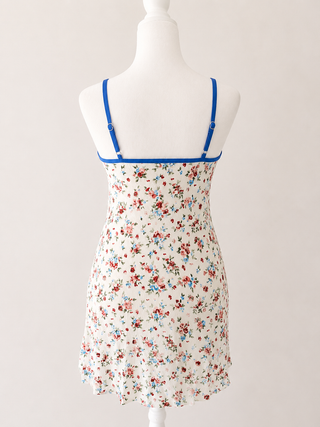 A sleeveless white slip dress with a red and blue floral print, featuring bright blue shoulder straps, displayed on a white mannequin torso against a light beige background.