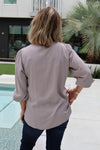 Person wearing a light gray blouse standing by a poolside with a building and palm tree in the background.