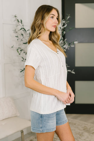 Woman wearing a white ribbed top and denim shorts in an indoor setting.