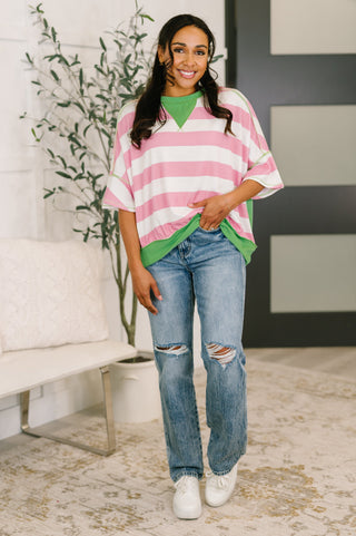 Woman wearing a pink and white striped sweater with green accents and ripped jeans indoors.