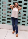 Woman posing against a teal brick wall wearing a white top and blue jeans.