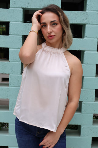 Woman wearing a light beige blouse against a light blue brick wall.