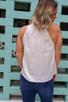 Person wearing a white halter top and blue jeans standing against a light blue brick wall.