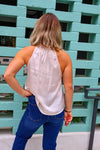 Person wearing a white sleeveless top and blue jeans standing against a teal brick wall.