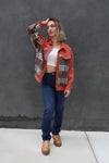 Woman wearing a red plaid jacket over a white top and blue jeans against a gray background