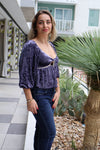 Woman wearing a purple top and blue jeans standing in front of a building with plants.